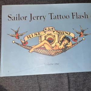 Sailor Jerry Tattoo Flash Volume 1 Author/Editor: Edited by the legendary Don Ed Hardy, featuring the Michael Malone Collection. Dimensions: Approximately 15 inches wide (38.74 x 28.58 cm). Length: 61 to 64 pages featuring full-size flash sheets. Content: Iconic American traditional motifs including pinups, eagles, ships, roses, hearts, and banners.